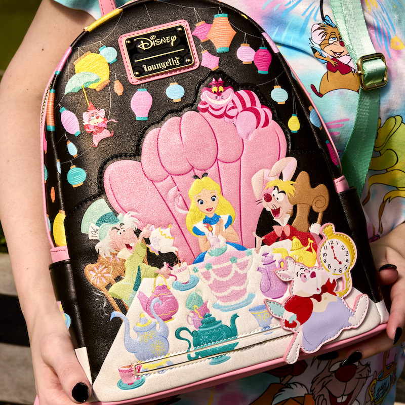 Person holding the Loungefly Alice in Wonderland Unbirthday Mini Backpack featuring Alice sitting in a pink chair at a table celebrating her unbirthday with the Cheshire Cat, the Mad Hatter, the March hare, the Dormouse, and the White Rabbit